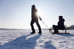 Two persons with sledge on frozen outer Alster in winter, Hamburg, Germany