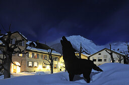Dog figure in front of illuminated Hotel Meisser, Guarda, Engadin, Grisons, Switzerland, Europe