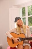 Adult, Adults, At home, Blonde, Blondes, Cap, Caps, Caucasian, Caucasians, Color, Color image, Colour, Contemporary, Daytime, Facing camera, Fair-haired, Female, grin, grinning, Guitar, Guitars, Hat, Hats, Headgear, Hobbies, Hobby, Home, human, indoor, in