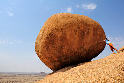 Woman pushing red balancing granite rock from slab, Great Spitzkoppe, Namibia