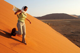 Frau läuft durch Sand von roter Sanddüne hinab, Düne 45, Sossusvlei, Namib Naukluft National Park, Namibwüste, Namib, Namibia
