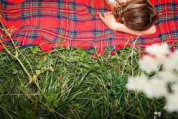 Junge Frau liegt auf einer rot karierten Decke im Gras