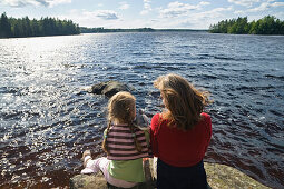 Mutter und Tochter sitzen auf Felsen am Store Hindsjön, Kalmar Län, Smaland, Schweden