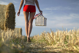 Junge Frau läuft mit einem Picknickkorb durch ein Stoppelfeld