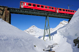 Zug der Rhätische Bahn fährt über Brücke durch Winterlandschaft zum Berninapass, UNESCO Weltkulturerbe Rhätische Bahn, Rhätische Bahn, Albula-Bernina-Linie, Berninabahn, Berninagruppe, Oberengadin, Engadin, Graubünden, Schweiz, Europa