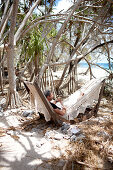 Gast in der Hängematte am Strand unter Pandanus Bäumen, Wilson Island Resort, Wilson Island, Teil des Capricornia Cays National Park, Great Barrier Reef Marine Park, UNESCO Weltnaturerbe, Queensland, Australien