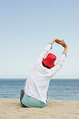 Woman wearing a red hut stretching at beach, List, Sylt, Schleswig-Holstein, Germany