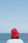 Woman wearing a red hut sitting at beach, List, Sylt, Schleswig-Holstein, Germany