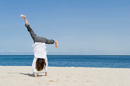 Woman turning cartwheels on sandy beach, List, Sylt, Schleswig-Holstein, Germany