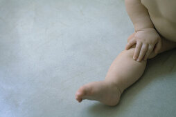 Nude baby sitting on the ground, hand on knee, cropped view