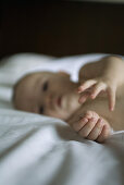 Baby lying on blanket, reaching towards camera, focus on hands
