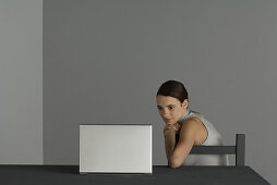 Woman sitting at table, watching laptop computer, hand under chin