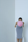 Woman bending over, holding balloon in mouth, looking at camera