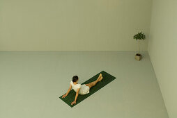 Woman sitting on artificial turf, looking at potted plant in corner, high angle view