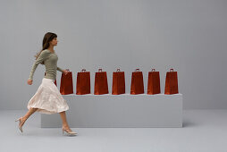 Woman walking past row of shopping bags, side view
