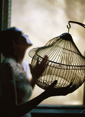 Woman standing beside window, holding empty birdcage