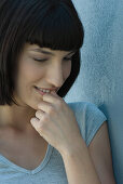 Young woman leaning against wall, biting nails, looking down