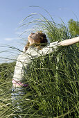 Woman standing with arms outstretched and head back in field of tall grass