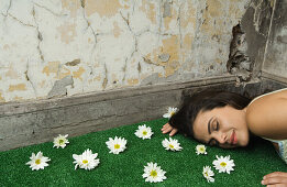 Woman lying on artificial turf scattered with flowers, surrounded by flaking walls