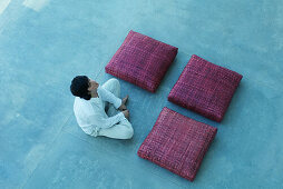 Three square cushions and man arranged in square shape, man crossing legs, closing eyes, high angle view