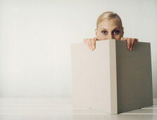 Woman peeking over edge of open book, looking at camera