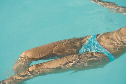 Woman floating on back in swimming pool, cropped