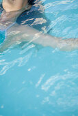 Woman floating in pool, cropped view