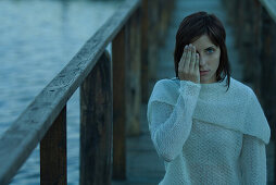 Woman covering one eye, standing on wooden pier, looking at camera