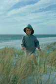 Boy running through dune grass, wearing hooded sweatshirt, full length
