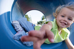 Close-up of girl reaching for camera, lying in playground tunnel