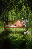 Junge Frau mit Buch auf Gartenbank, Simssee, Bayern, Deutschland