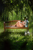 Young woman reading a book on a garden bench, Simssee, Bavaria, Germany