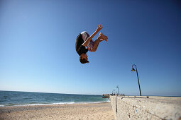 Junger Mann springt von Hafenmauer am Castillo de San Sebastian, Calle de Fernando Quiñones, Cádiz, Spanien