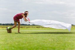 Young woman setting a sheet on the grass, oudoors