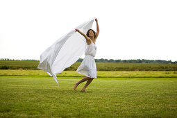Young woman running with white sheet, oudoors