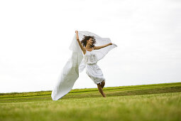 Young woman running with a white sheet , oudoors