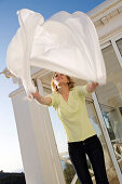 Young woman shaking tablecloth, outdoors