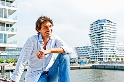 Mann mittleren Alters lächelt, Marco-Polo-Tower im Hintergrund, HafenCity, Hamburg, Deutschland