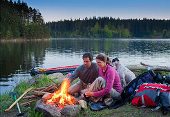 Young couple sitting around a campfire at dusk, lake Ottenstein, Lower Austria, Austria, Europe