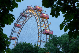 View through trees onto illuminated ferris wheel, Prater, 2. Bezirk, Leopoldstadt, Vienna, Austria, Europe