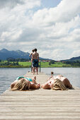 Zwei Mädchen sonnen sich auf einem Steg am Hopfensee, Füssen, Allgäu, Bayern, Deutschland