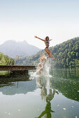 Two teenage girls jumping into lake Schwansee, Schwangau, Allgaeu, Bavaria, Germany