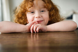 Little girl resting her arms on a coffee table, looking at the camera