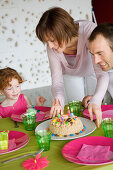 Couple and little girl with birthday cake at lunch table