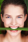 Young smiling woman holding plants between teeth