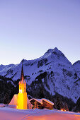 Beleuchtete Kirche vor Bergkulisse, Schröcken, Vorarlberg, Österreich