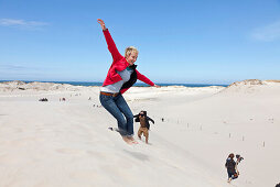 Leba Dunes, young woman jumping into the dunes, view towards the sea, UNESCO World Biosphere Reserve, Slowinski National Park, Polish Baltic Sea coast, MR, Leba, Pomeranian, Poland