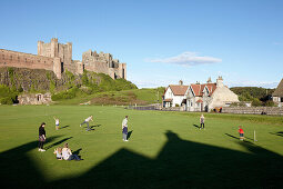 Menschen spielen auf einem Cricketfeld unterhalb Bamburgh Castle, Bamburgh, Northumberland, England, Grossbritannien, Europa