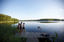 Family on jetty, woman jumping into lake Goldensee, Klein Thurow, Roggendorf, Mecklenburg-Western Pomerania, Germany