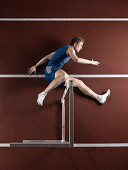 Runner laying with hurdle on track. Athlete jumping over hurdle, lying on track and field stadium